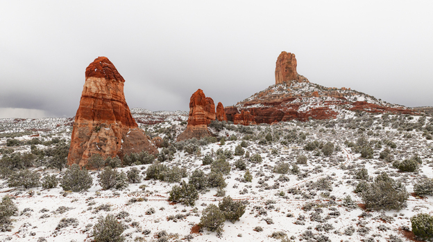 Aerial view of towering red sandstone buttes and rock formations rising from a snow covered desert landscape with green shrubs under an overcast sky in Page Arizona United States.