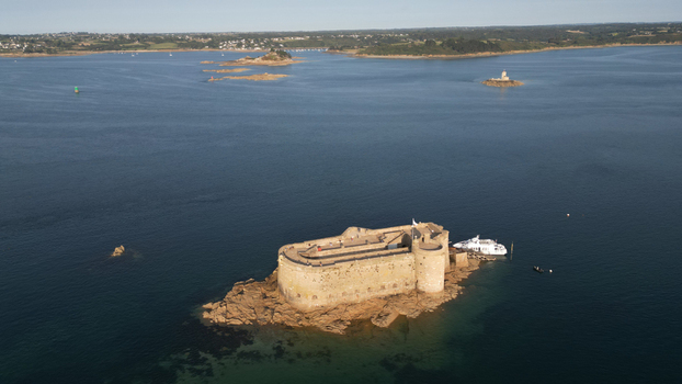 Aerial view of the imposing Ch&acirc;teau du Taureau bathed in sunlight standing sentinel in the tranquil bay a stark contrast to the deep blue sea Plouezoc h Bretagne France.