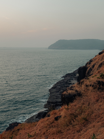 View of the rugged coastline where golden grasses meet the turquoise sea under a hazy sky a tranquil escape into nature s embrace Chiplun Maharashtra India. View of the rugged coastline where golden grasses meet the turquoise sea under a hazy sky a tranquil escape into nature s embrace Chiplun Maharashtra India.