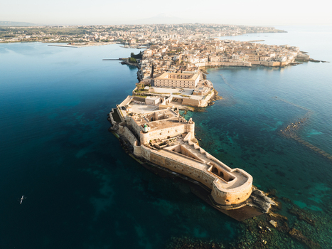 Aerial view of the Island of Ortigia featuring Maniace Castle surrounded by the blue Mediterranean Sea in Syracuse Sicily Italy. Aerial view of the Island of Ortigia featuring Maniace Castle surrounded by the blue Mediterranean Sea in Syracuse Sicily Italy.