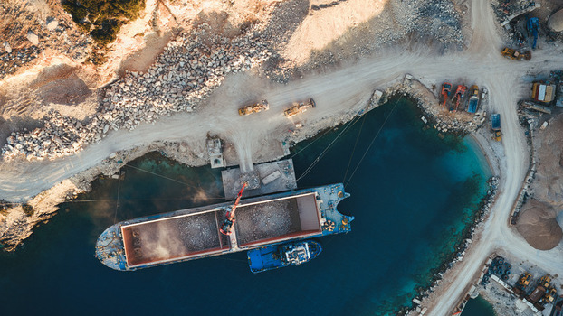 Aerial view of the Jadrankamen stone quarry with a cargo ship being loaded by heavy machinery and excavators on the coast in Pucisca Splitsko dalmatinska Croatia. Aerial view of the Jadrankamen stone quarry with a cargo ship being loaded by heavy machinery and excavators on the coast in Pucisca Splitsko dalmatinska Croatia.