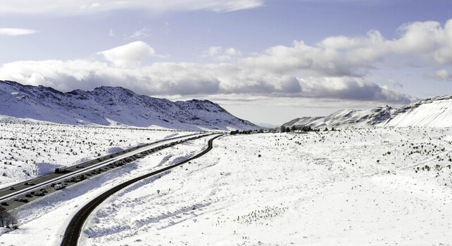 Aerial view of a snow covered highway winding through mountainous terrain with traffic and clear blue sky in Lancaster CA United States.