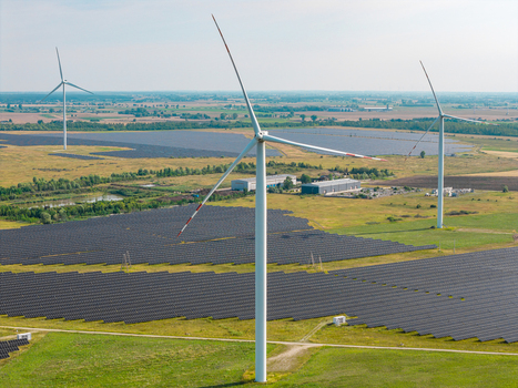 Aerial view of a wind and solar farm featuring large wind turbines and extensive solar panel arrays set in a rural landscape in Poland.