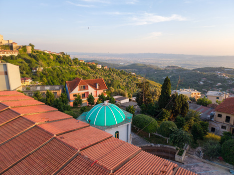 Aerial view of the historic town of Kruje with red tiled rooftops a vibrant green dome and lush green hillsides overlooking a vast valley in Kruje Durres County Albania.