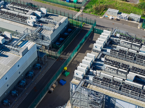 Aerial view of a modern data center facility featuring rows of industrial cooling units on rooftops secure perimeter fencing and paved access paths United Kingdom.