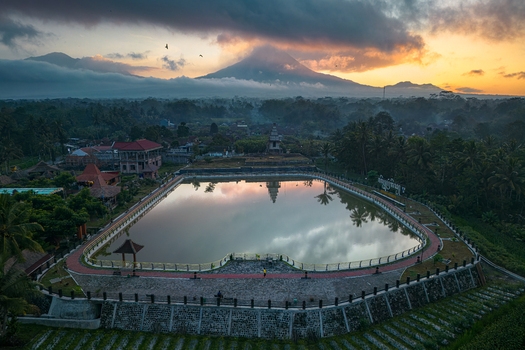 Aerial view of Embung Mranggen reservoir reflecting the sky with Mount Merapi volcano under a dramatic sunrise in Magelang Central Java Indonesia.