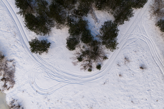 Aerial view of winding tire tracks on a snow covered field next to a cluster of evergreen trees in Lithuania. Aerial view of winding tire tracks on a snow covered field next to a cluster of evergreen trees in Lithuania.