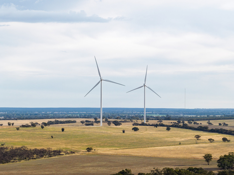Aerial view of two wind turbines standing in a vast dry rural landscape with scattered trees and fields under a cloudy sky in Kiata Victoria Australia. Aerial view of two wind turbines standing in a vast dry rural landscape with scattered trees and fields under a cloudy sky in Kiata Victoria Australia.