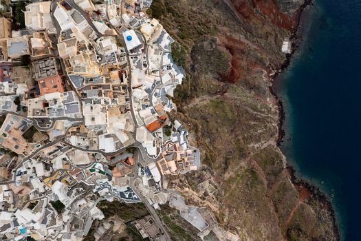 Aerial view of whitewashed buildings cascade down the cliffs towards the azure sea a striking contrast against the volcanic landscape Fira Thira Greece. Aerial view of whitewashed buildings cascade down the cliffs towards the azure sea a striking contrast against the volcanic landscape Fira Thira Greece.