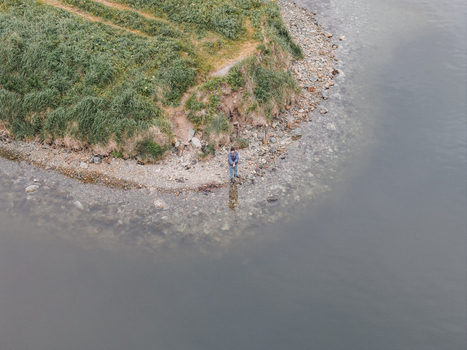 Aerial view of a person standing on the rocky shoreline of a bay in Unalaska Alaska United States.