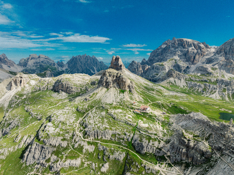 Aerial view of the iconic Tre Cime di Lavaredo peaks surrounded by green alpine meadows and rocky trails in Auronzo di Cadore Veneto Italy.
