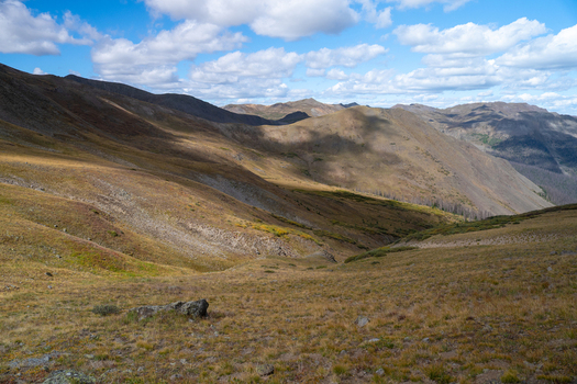 View of San Luis Peak and the rugged mountain landscape near West Willow Creek Trailhead with golden grassy slopes and shadows under a blue sky in Creede Colorado United States. View of San Luis Peak and the rugged mountain landscape near West Willow Creek Trailhead with golden grassy slopes and shadows under a blue sky in Creede Colorado United States.