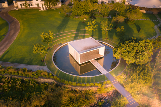 Aerial view of a modern white pavilion centered in a circular pond surrounded by lush green gardens and trees during golden hour in Cape Town Western Cape South Africa. Aerial view of a modern white pavilion centered in a circular pond surrounded by lush green gardens and trees during golden hour in Cape Town Western Cape South Africa.