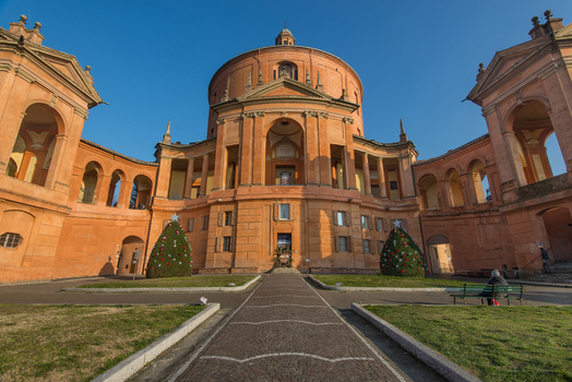 View of Santuario Madonna di San Luca historic circular basilica with its distinctive orange facade porticoes and Christmas trees in the courtyard Bologna Emilia Romagna Italy. View of Santuario Madonna di San Luca historic circular basilica with its distinctive orange facade porticoes and Christmas trees in the courtyard Bologna Emilia Romagna Italy.