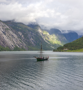 Aerial view of Hardangerfjord with a traditional wooden sailing ship surrounded by steep misty mountains and calm water Blurnes Vestland Norway. Aerial view of Hardangerfjord with a traditional wooden sailing ship surrounded by steep misty mountains and calm water Blurnes Vestland Norway.