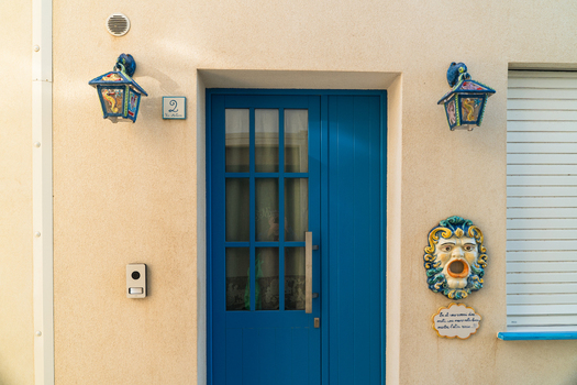 View of a vibrant blue wooden door with glass panes decorative lanterns and a ceramic mask on a beige wall in Marsaskala Southern Region Malta. View of a vibrant blue wooden door with glass panes decorative lanterns and a ceramic mask on a beige wall in Marsaskala Southern Region Malta.