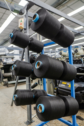View of black yarn spools arranged on a blue metal rack in a denim factory production line in Karachi Sindh Pakistan. View of black yarn spools arranged on a blue metal rack in a denim factory production line in Karachi Sindh Pakistan.