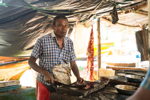 Sri Lanka 04 February 2026 View of a local fisherman cutting fresh fish on a wooden block inside a rustic market stall with a black tarp roof.