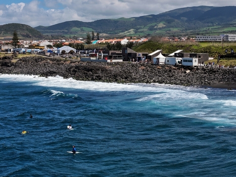 Aerial view of surfers in the blue waves of Praia do Areal de Santa Barbara with dark volcanic rocks and green hills in Ribeira Grande Acores Portugal. Aerial view of surfers in the blue waves of Praia do Areal de Santa Barbara with dark volcanic rocks and green hills in Ribeira Grande Acores Portugal.