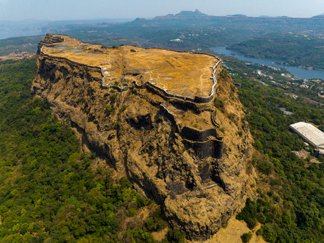 Aerial view of Korigad Fort with its historic stone fortifications and dry grassy plateau surrounded by lush green forests and a distant lake in Peth Shahapur Maharashtra India. Aerial view of Korigad Fort with its historic stone fortifications and dry grassy plateau surrounded by lush green forests and a distant lake in Peth Shahapur Maharashtra India.