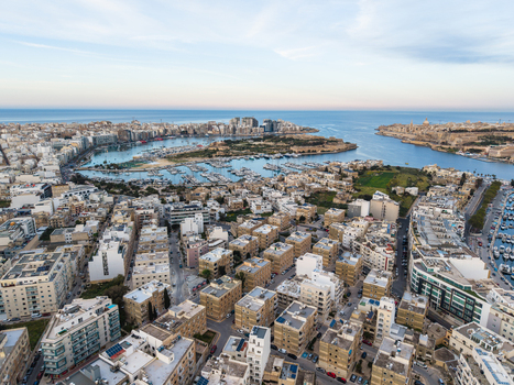 Aerial view of dense urban residential buildings and a harbor filled with yachts under a clear blue sky in Malta. Aerial view of dense urban residential buildings and a harbor filled with yachts under a clear blue sky in Malta.