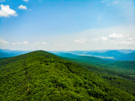 Lost City West Virginia United States 12 June 2019 Aerial view of the lush green forested mountains of the Appalachian range under a bright blue sky with scattered white clouds. Lost City West Virginia United States 12 June 2019 Aerial view of the lush green forested mountains of the Appalachian range under a bright blue sky with scattered white clouds.