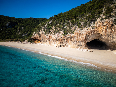 Aerial view of Cala Luna beach with turquoise water white sand and limestone caves under a clear blue sky in Baunei Sardegna Italy. Aerial view of Cala Luna beach with turquoise water white sand and limestone caves under a clear blue sky in Baunei Sardegna Italy.