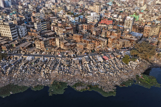 Aerial view of the Buriganga River bank featuring dense urban housing and numerous white sacks piled along the waterfront in Dhaka Dhaka Division Bangladesh. Aerial view of the Buriganga River bank featuring dense urban housing and numerous white sacks piled along the waterfront in Dhaka Dhaka Division Bangladesh.