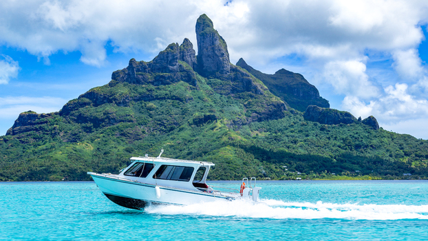 View of a white motorboat cruising across the turquoise lagoon with the lush green slopes of Mount Otemanu in the background Bora Bora Leeward Islands French Polynesia.