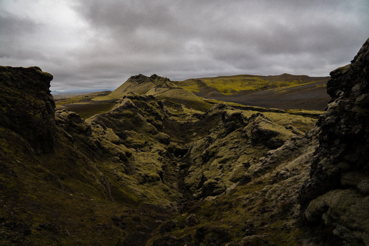 View of mossy rocks and grassy hills under a cloudy sky with dark volcanic sand stretching to the horizon Skaftárhreppur Skaftárhreppur Iceland. View of mossy rocks and grassy hills under a cloudy sky with dark volcanic sand stretching to the horizon Skaftárhreppur Skaftárhreppur Iceland.