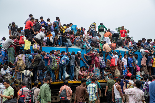 Dhaka Bangladesh 15 June 2018 View of Airport Railway Station with a massive crowd of passengers climbing and sitting on the roof of a blue train during the Eid holiday rush. Dhaka Bangladesh 15 June 2018 View of Airport Railway Station with a massive crowd of passengers climbing and sitting on the roof of a blue train during the Eid holiday rush.