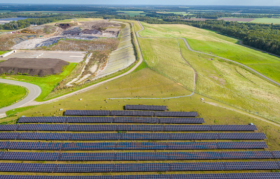 Aerial view of solar panels installed on a grassy slope adjacent to a large landfill site with waste management infrastructure in Wijster Drenthe Netherlands.