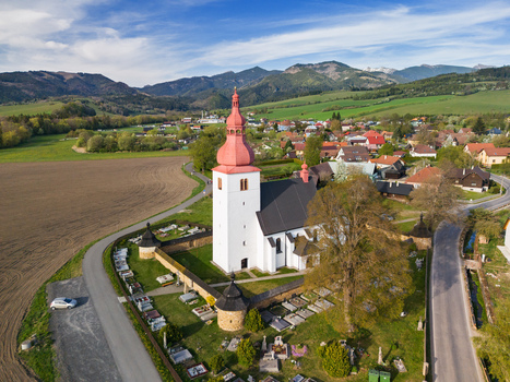 Aerial view of the historic Church of Saint Ladislaus featuring a red onion dome and fortified walls surrounded by a cemetery and green fields in Liptovske Matiasovce Zilina Region Slovakia.