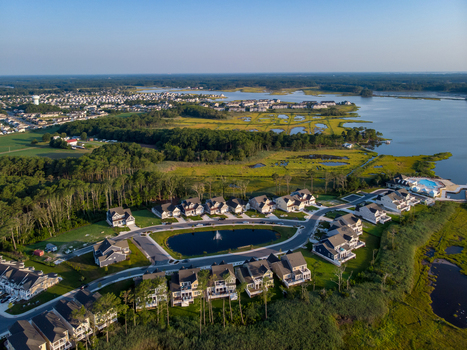 Ocean City Maryland United States 28 July 2019 Aerial view of a residential neighborhood with houses surrounding a central pond set against coastal wetlands and a bay.