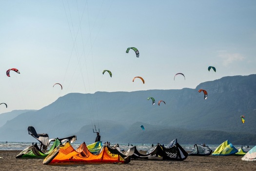 View of colorful kites flying over the beach with kite surfers and mountains in the background in Akyaka Mugla Turkey. View of colorful kites flying over the beach with kite surfers and mountains in the background in Akyaka Mugla Turkey.