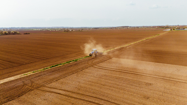 Aerial view of a tractor churning the rich brown earth dust billowing against the pale sky contrasting with the green strip Sremska Mitrovica Vojvodina Serbia. Aerial view of a tractor churning the rich brown earth dust billowing against the pale sky contrasting with the green strip Sremska Mitrovica Vojvodina Serbia.