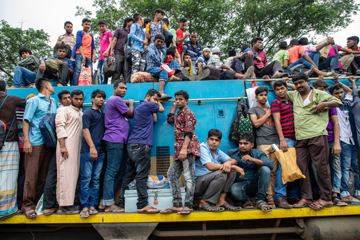 Dhaka Bangladesh 15 June 2018 View of crowds of people sitting on the roof and clinging to the side of a blue train at Airport Railway Station. Dhaka Bangladesh 15 June 2018 View of crowds of people sitting on the roof and clinging to the side of a blue train at Airport Railway Station.