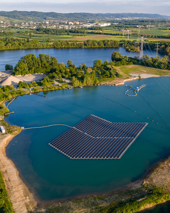 Aerial view of floating solar panels on a lake surrounded by lush greenery and power lines in Bensheim Hessen Germany. Aerial view of floating solar panels on a lake surrounded by lush greenery and power lines in Bensheim Hessen Germany.