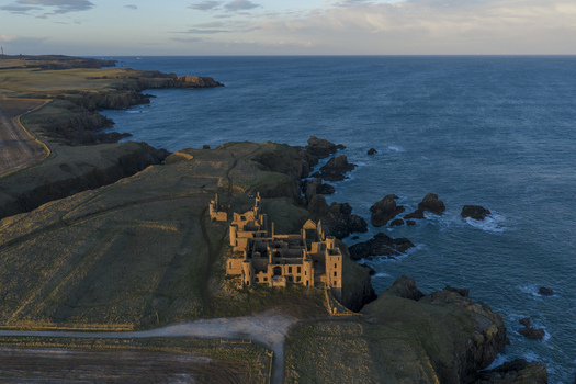 Aerial view of Slains Castle ruined stone walls on a rugged cliff edge overlooking the North Sea during golden hour in Cruden Bay Scotland United Kingdom. Aerial view of Slains Castle ruined stone walls on a rugged cliff edge overlooking the North Sea during golden hour in Cruden Bay Scotland United Kingdom.