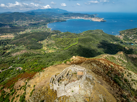 Aerial view of the historic Castello del Volterraio ruins perched on a rocky hilltop overlooking the lush green landscape and the blue bay of Portoferraio Toscana Italy.
