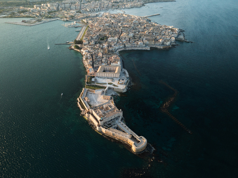 Aerial view of the historic Island of Ortigia featuring Maniace Castle and dense stone architecture surrounded by the deep blue Ionian Sea Syracuse Sicily Italy. Aerial view of the historic Island of Ortigia featuring Maniace Castle and dense stone architecture surrounded by the deep blue Ionian Sea Syracuse Sicily Italy.