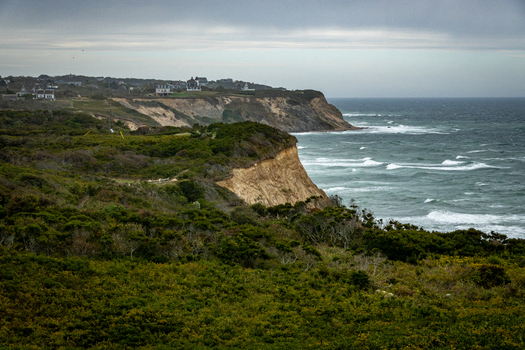 View of Block Island featuring dramatic coastal cliffs lush green vegetation crashing waves and houses perched on the shoreline in New Shoreham Rhode Island United States.