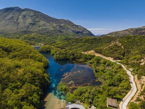 Aerial view of the Blue Eye natural spring with its vibrant deep blue water surrounded by lush green forests rolling hills and a scenic walking path in Finiq Vlore County Albania. Aerial view of the Blue Eye natural spring with its vibrant deep blue water surrounded by lush green forests rolling hills and a scenic walking path in Finiq Vlore County Albania.