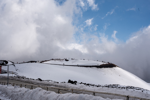 View of a snow covered landscape under a cloudy sky with people visible atop a distant peak creating a stark contrast between white and blue Taormina Sicily Italy.