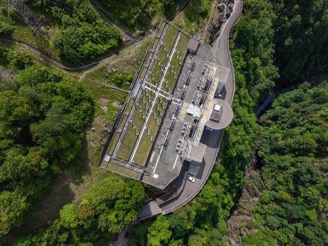 Aerial view of the Verzasca Dam electrical substation surrounded by lush green forests and a winding mountain road in Gordola Ticino Switzerland. Aerial view of the Verzasca Dam electrical substation surrounded by lush green forests and a winding mountain road in Gordola Ticino Switzerland.