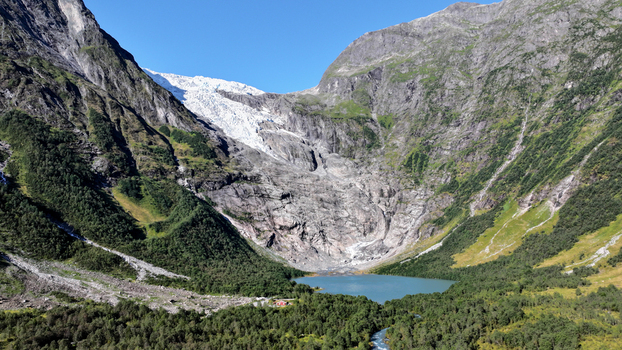 Aerial view of a glacier nestled between steep mountain slopes above a turquoise glacial lake surrounded by lush green forests Nordland Norway. Aerial view of a glacier nestled between steep mountain slopes above a turquoise glacial lake surrounded by lush green forests Nordland Norway.