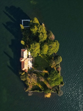 Aerial view of the small private island of San Paolo on Lake Iseo with its historic villa lush green gardens and tall cypress trees casting long shadows in Monte Isola Lombardy Italy. Aerial view of the small private island of San Paolo on Lake Iseo with its historic villa lush green gardens and tall cypress trees casting long shadows in Monte Isola Lombardy Italy.