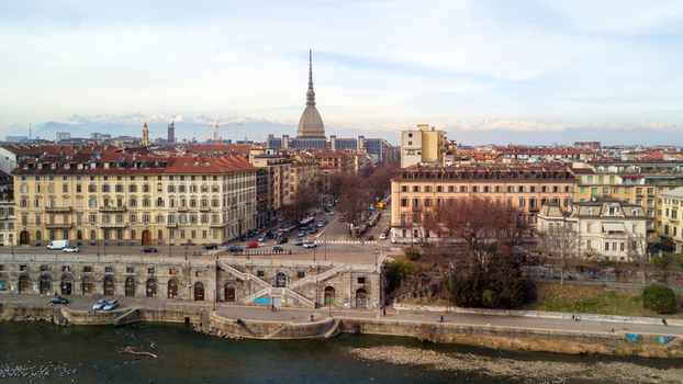 Aerial view of the Mole Antonelliana rising above the city skyline with the Po River in the foreground and snow capped Alps in the distance Turin Piedmont Italy.
