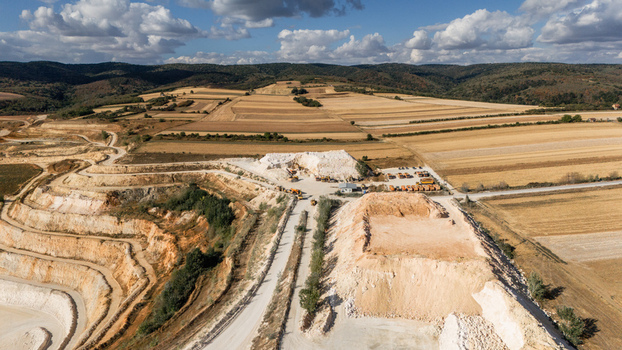 Aerial view of the Besenovo quarry featuring exposed limestone layers heavy machinery and surrounding agricultural fields under a cloudy sky in Besenovo Vojvodina Serbia. Aerial view of the Besenovo quarry featuring exposed limestone layers heavy machinery and surrounding agricultural fields under a cloudy sky in Besenovo Vojvodina Serbia.