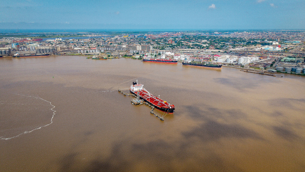 Aerial view of a large oil tanker docked at a terminal in the harbor with industrial port facilities and the city skyline in the background in Lagos Lagos Nigeria.
